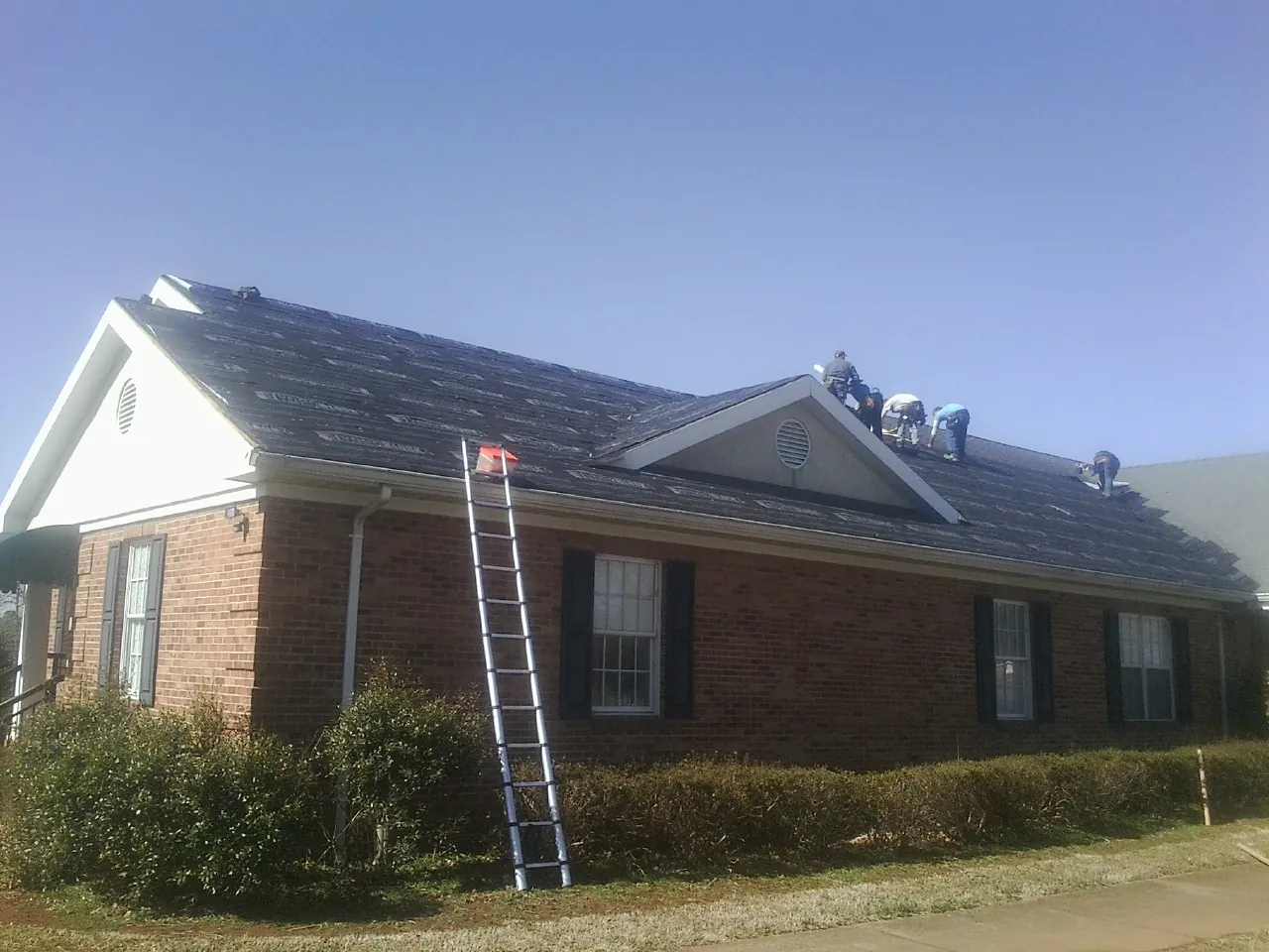Crew tearing shingles off a brick ranch roof with a ladder set — Metal Roof Repair work by our crew in Middletown